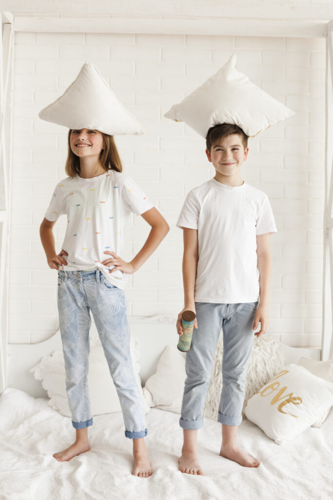 smiling-sibling-standing-with-pillow-their-head-bedroom